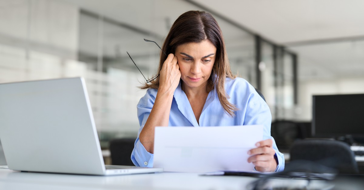 A person sitting in a large office looking disappointed as they glance down at a piece of paper in their hands.