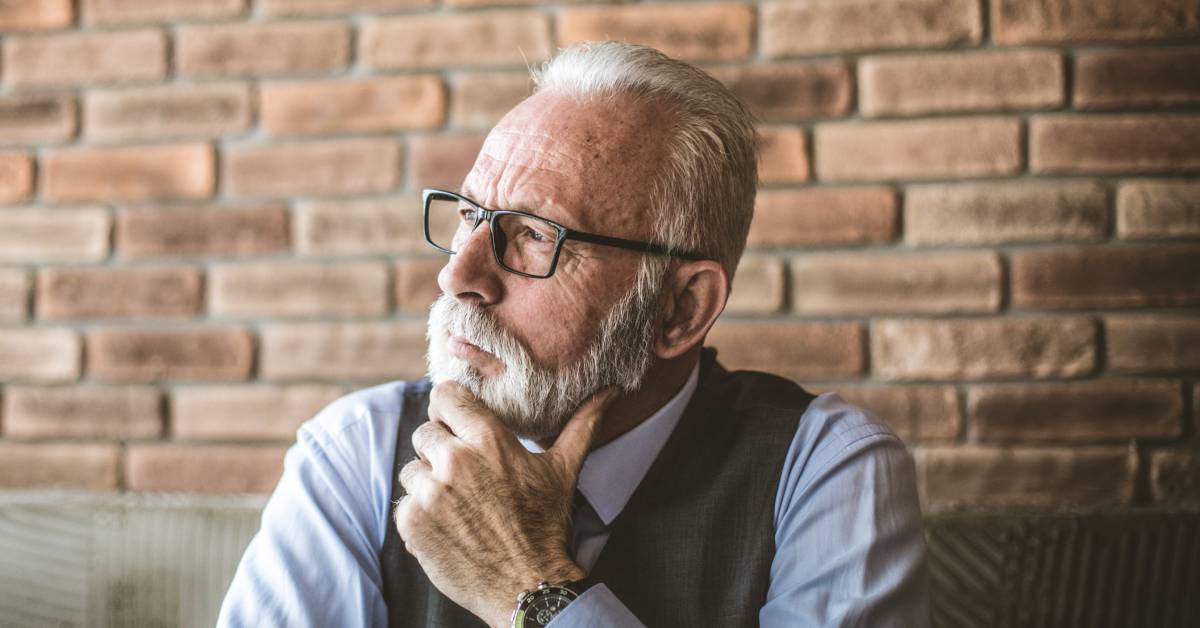 A person wearing a watch and glasses is looking to their right while sitting in front of a brick wall.