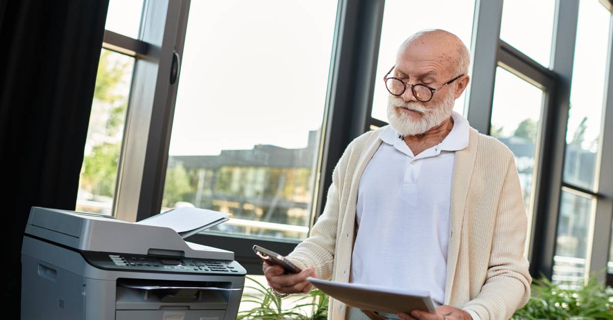 A person wearing glasses is holding a cell phone in their right hand and a notebook in their left hand.