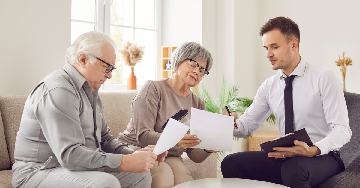 Two people sitting on a couch and holding paper documents, while a third person points to a document with a pen.